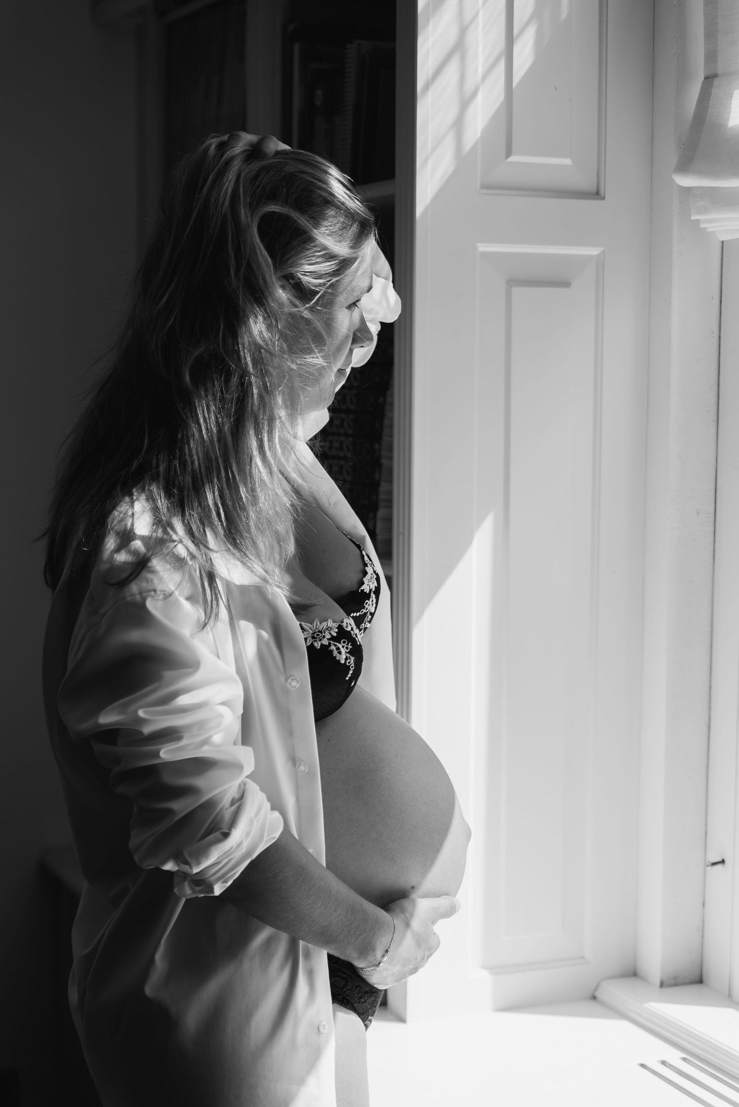 A silhouette of a pregnant woman standing by a window in dramatic lighting.