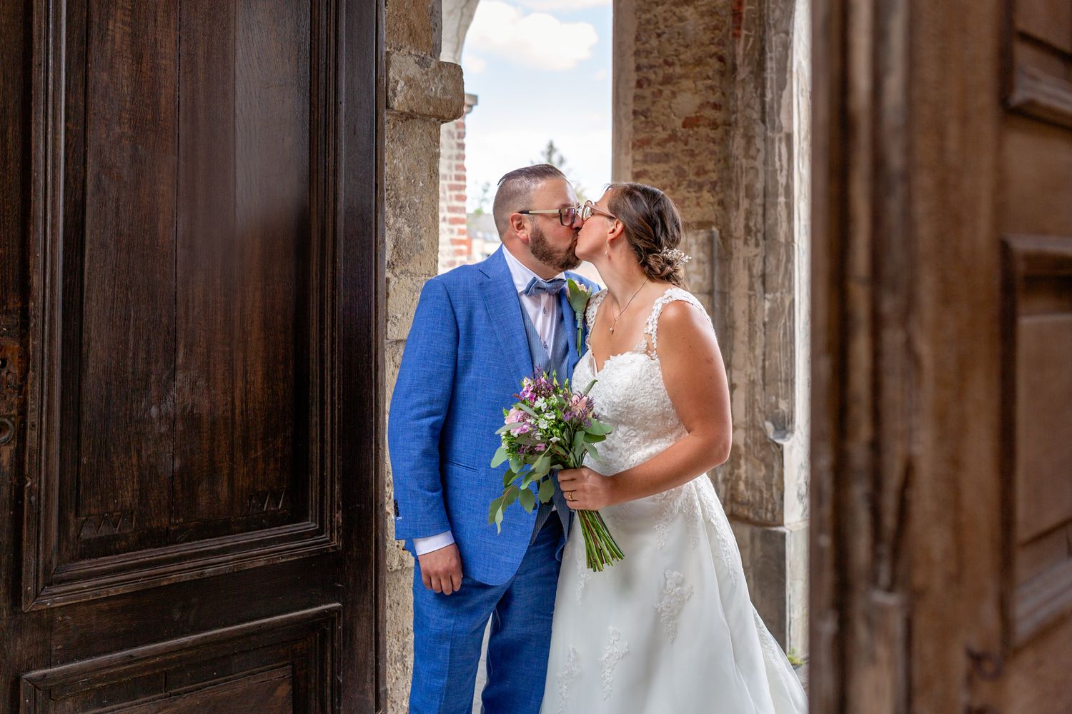 A romantic wedding photo of newlyweds standing in a rustic doorway with stone architecture.