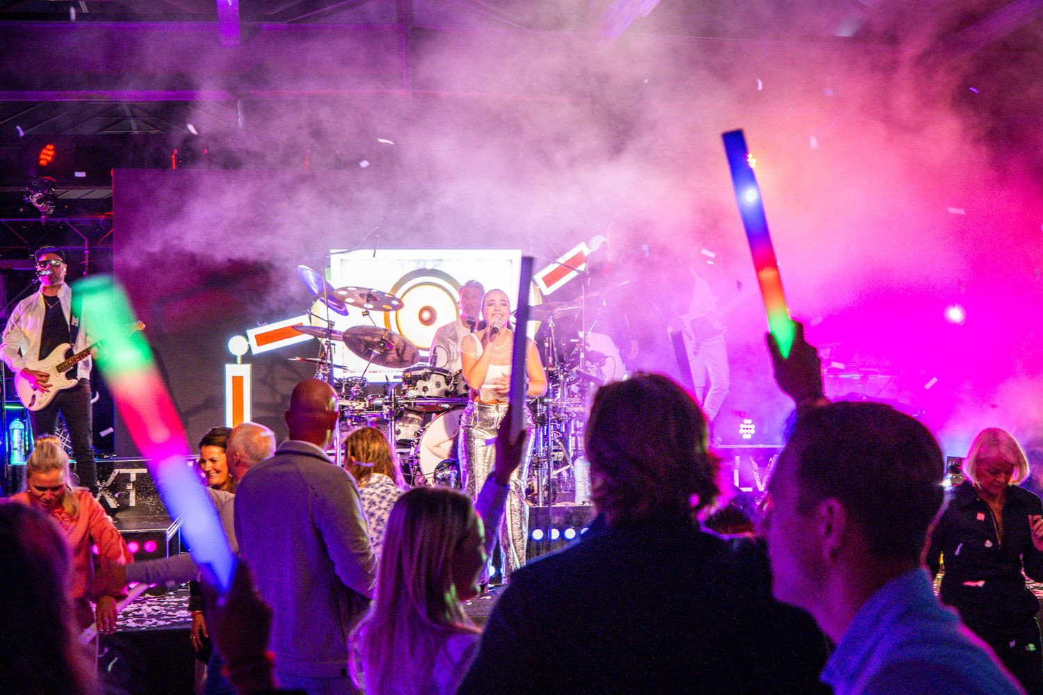 Feestende menigte met lichtstaven in kleurrijke rook tijdens liveconcert.