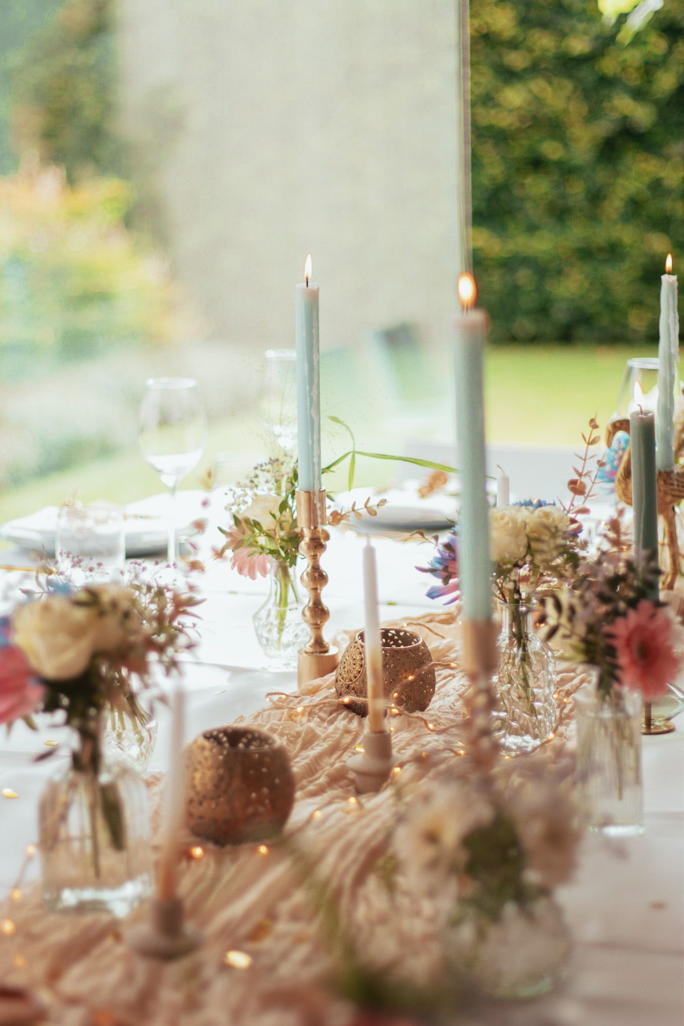 21-diner in de tuin: versierde tafel met bloemen en blauwe kaarsen in kandelaars, klaar voor een feestelijke avond.