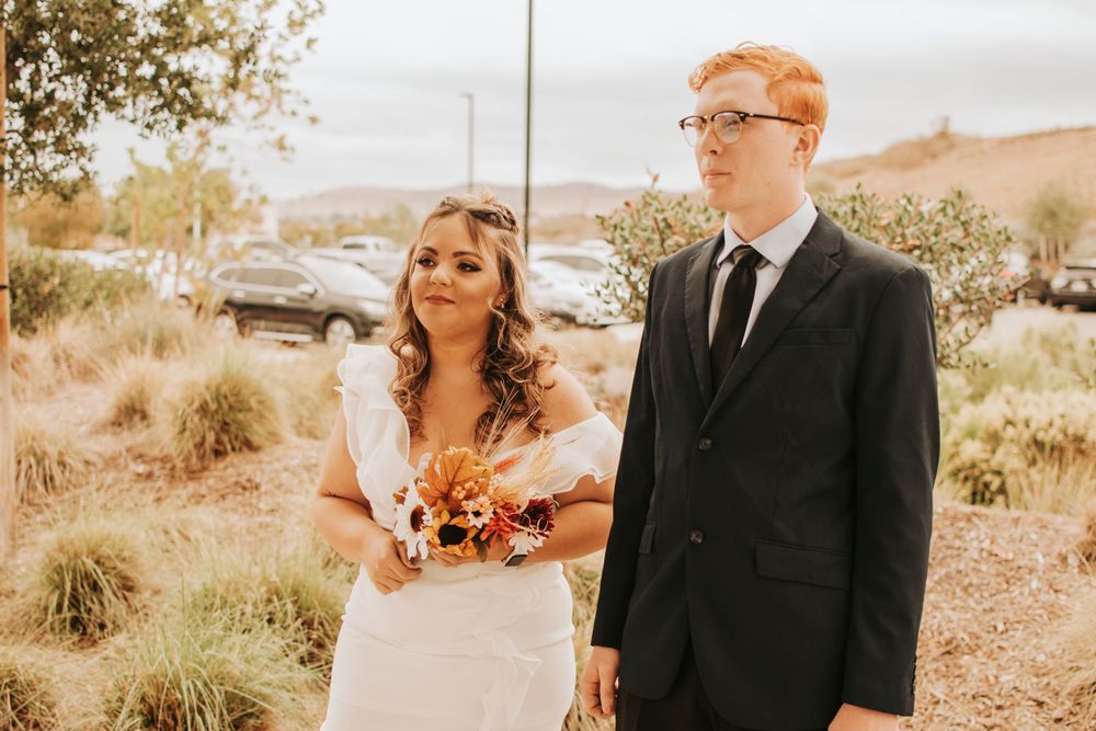 Couple in wedding attire sharing a moment in sunlit outdoor setting.