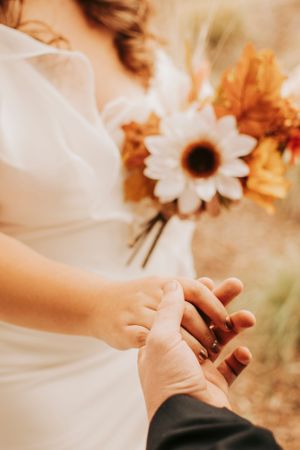 Close-up of hands exchanging rings during a wedding ceremony with sunflowers in the background.