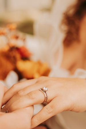 Close-up detail of an engagement ring with orange floral bouquet in soft focus background.