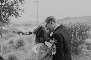 Black and white photo of a romantic wedding kiss in an outdoor garden setting.