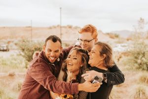 Group of wedding guests sharing a joyful embrace outdoors with desert landscape in background.