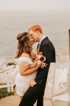 Romantic sunset wedding portrait of couple embracing on coastal stairs with fall bouquet.
