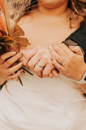Close-up of newlyweds' hands holding dried flowers and showing wedding rings.