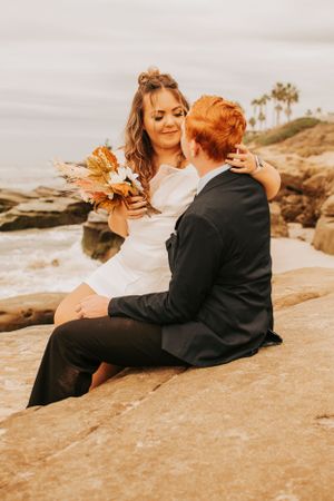 A couple shares a tender moment while sitting on coastal rocks during their wedding.