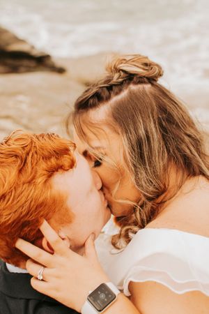 An intimate wedding portrait shows a couple sharing a kiss on the beach.
