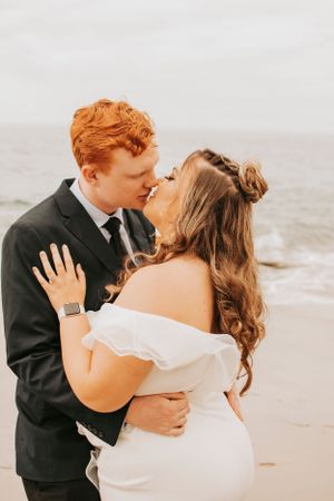 A romantic beach wedding photo showing a couple embracing in formal attire against an ocean backdrop.