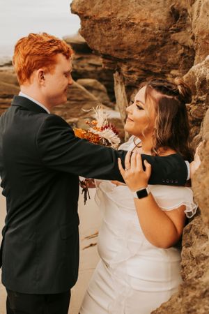 An intimate wedding moment captured between a couple near rocky cliffs by the ocean.