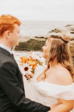 A seaside wedding photo with sunflowers and formal attire against coastal rocks.