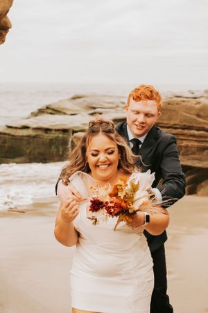 A candid wedding moment with autumn flowers against dramatic coastal rocks.
