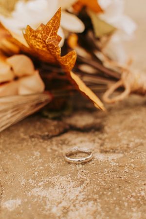 Close-up of a delicate wedding ring with autumn leaves and dried flowers in warm golden tones.