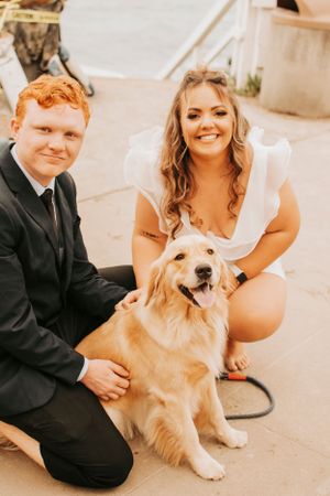 Happy couple posing with their friendly golden retriever in formal attire.