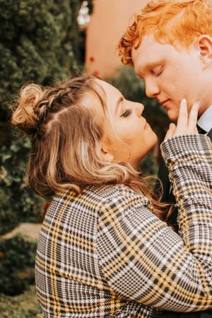 Intimate moment captured between couple wearing plaid coat against natural greenery.