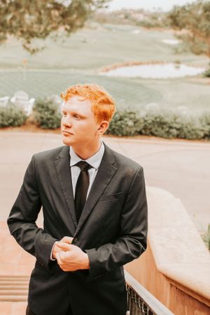A person in a dark suit and tie looks away thoughtfully during a portrait session outdoors.