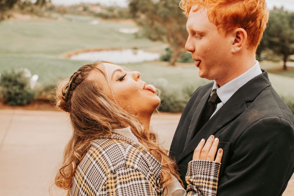 Couple in formal wear sharing a candid moment outdoors in warm sunlight.