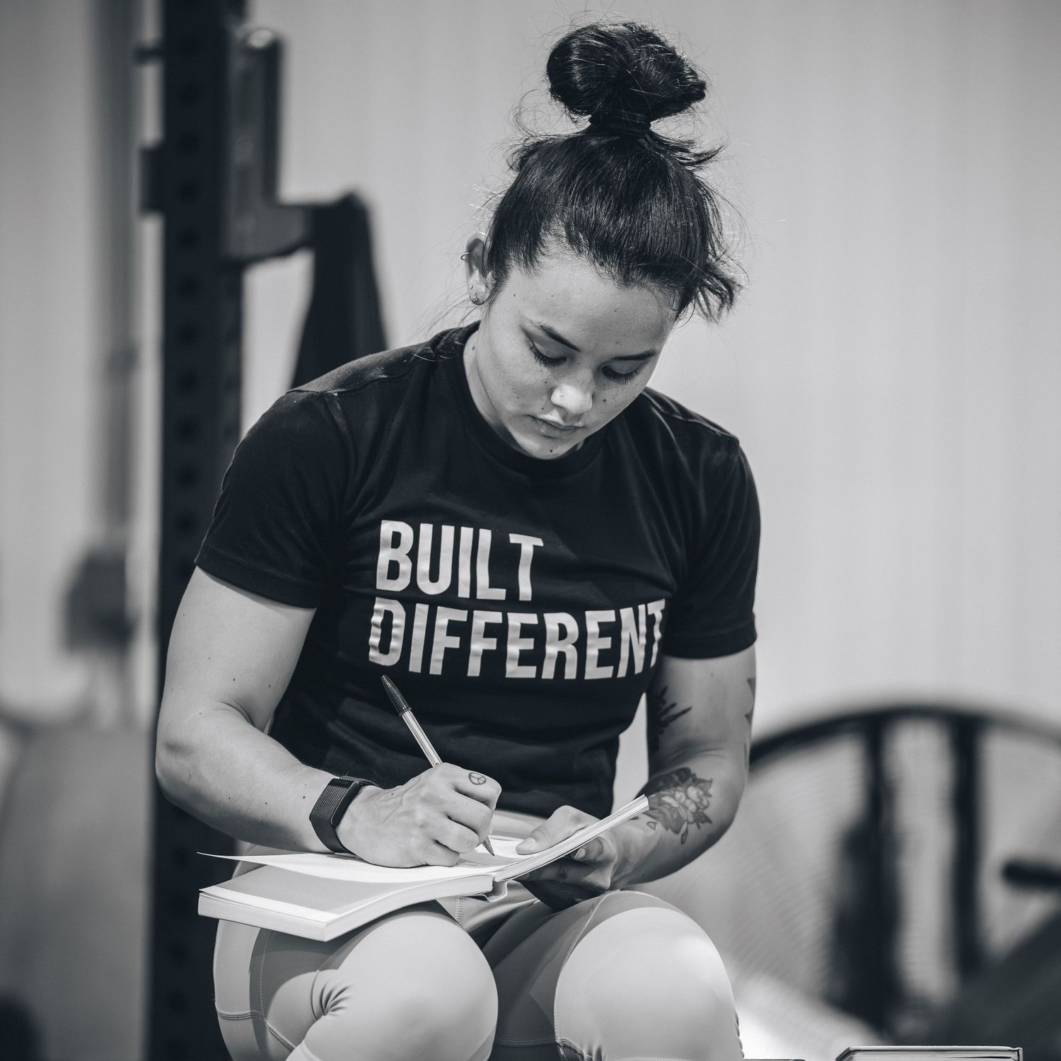 Athlete in 'Built Different' t-shirt writing in notebook during training session.