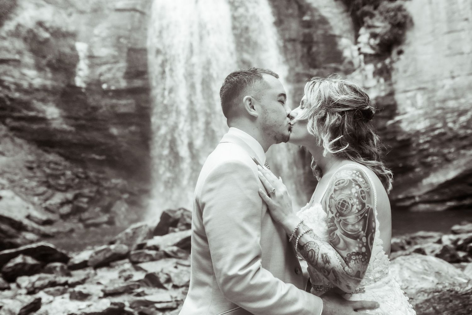 Black and white image of a man and woman kissing in front of waterfall after elopement in Asheville.