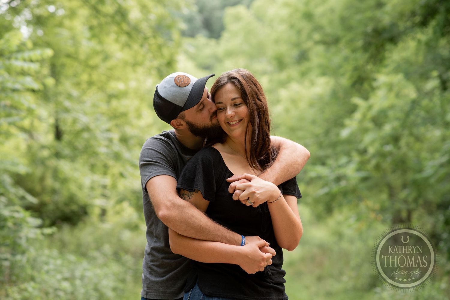 A romantic couple shares a tender embrace while dancing on a green nature trail.