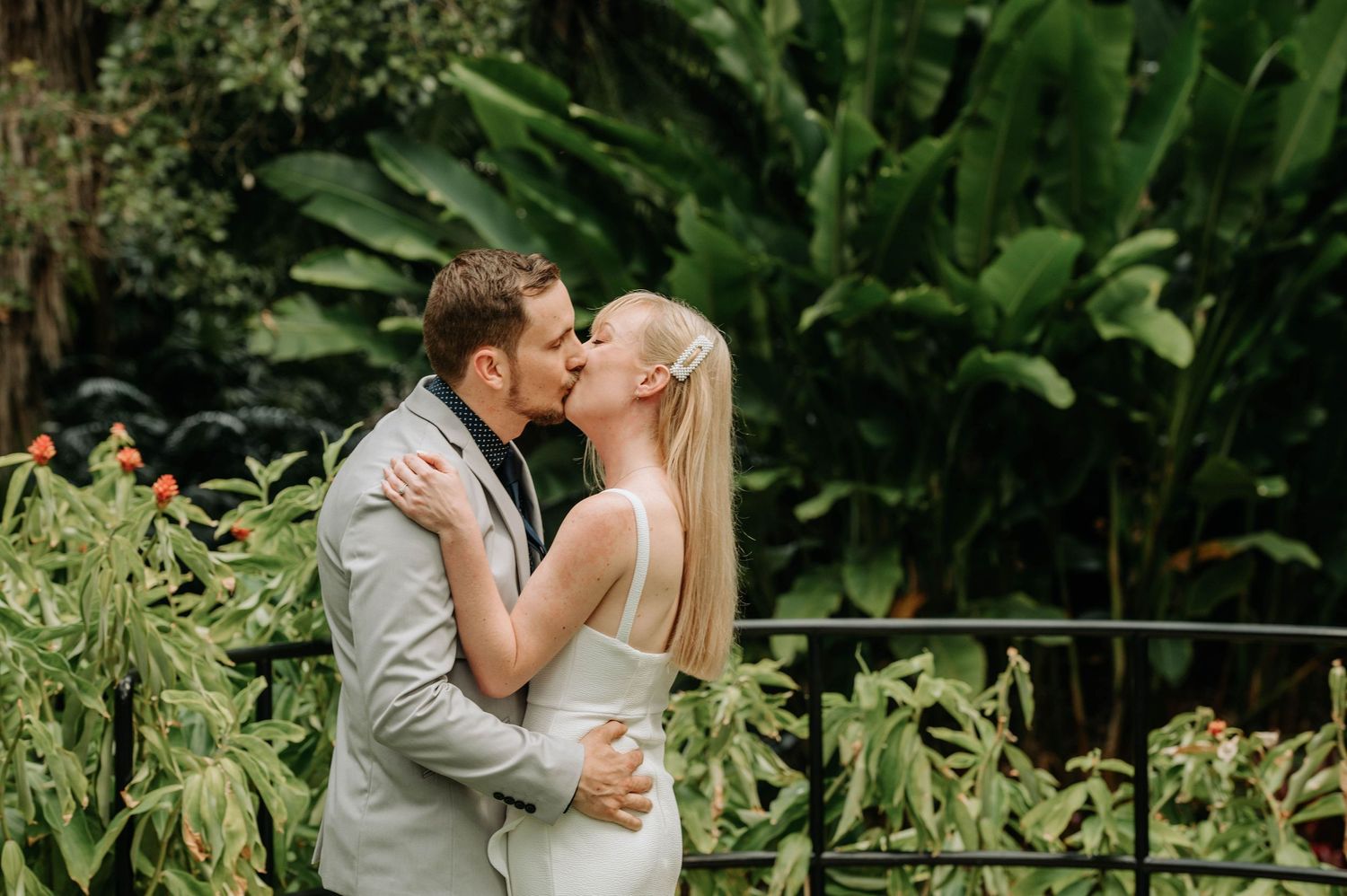 Romantic moment between newlyweds surrounded by tropical garden foliage.
