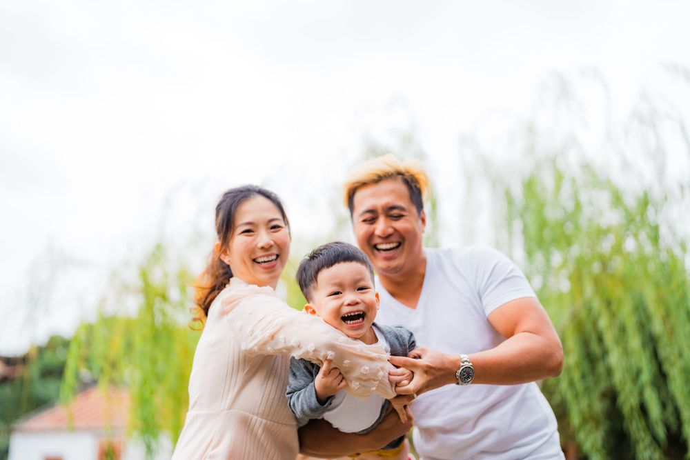 Joyful family moment captured outdoors with laughter and smiles against willow tree background.