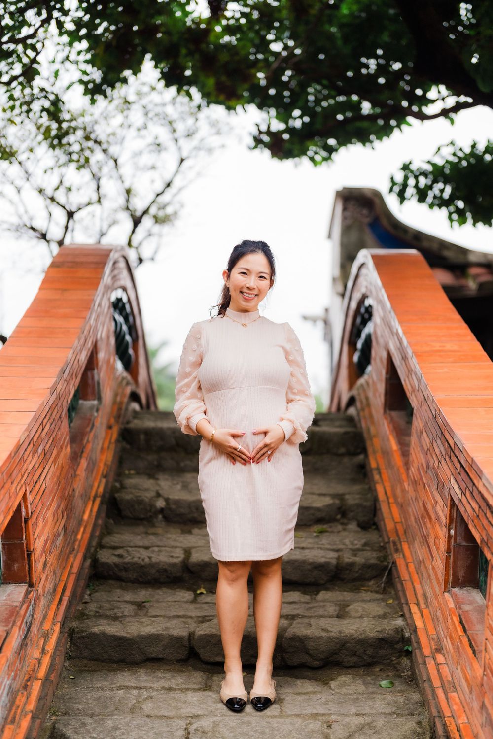 Woman in beige dress standing on orange wooden stairs in a garden setting.