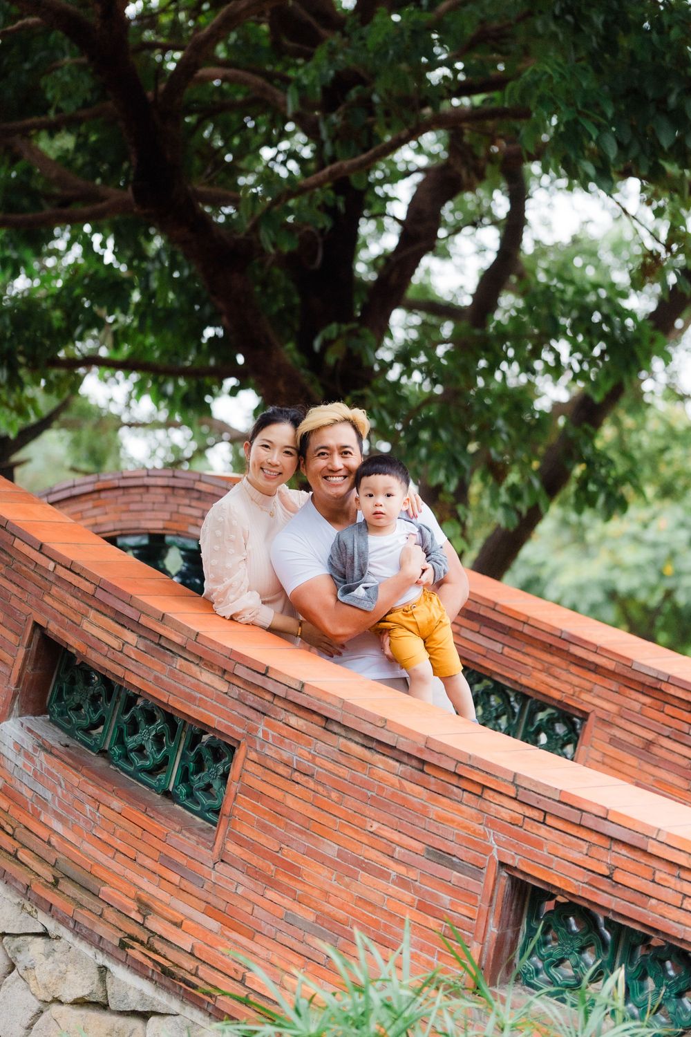 Family poses together on decorative brick steps under lush green trees.