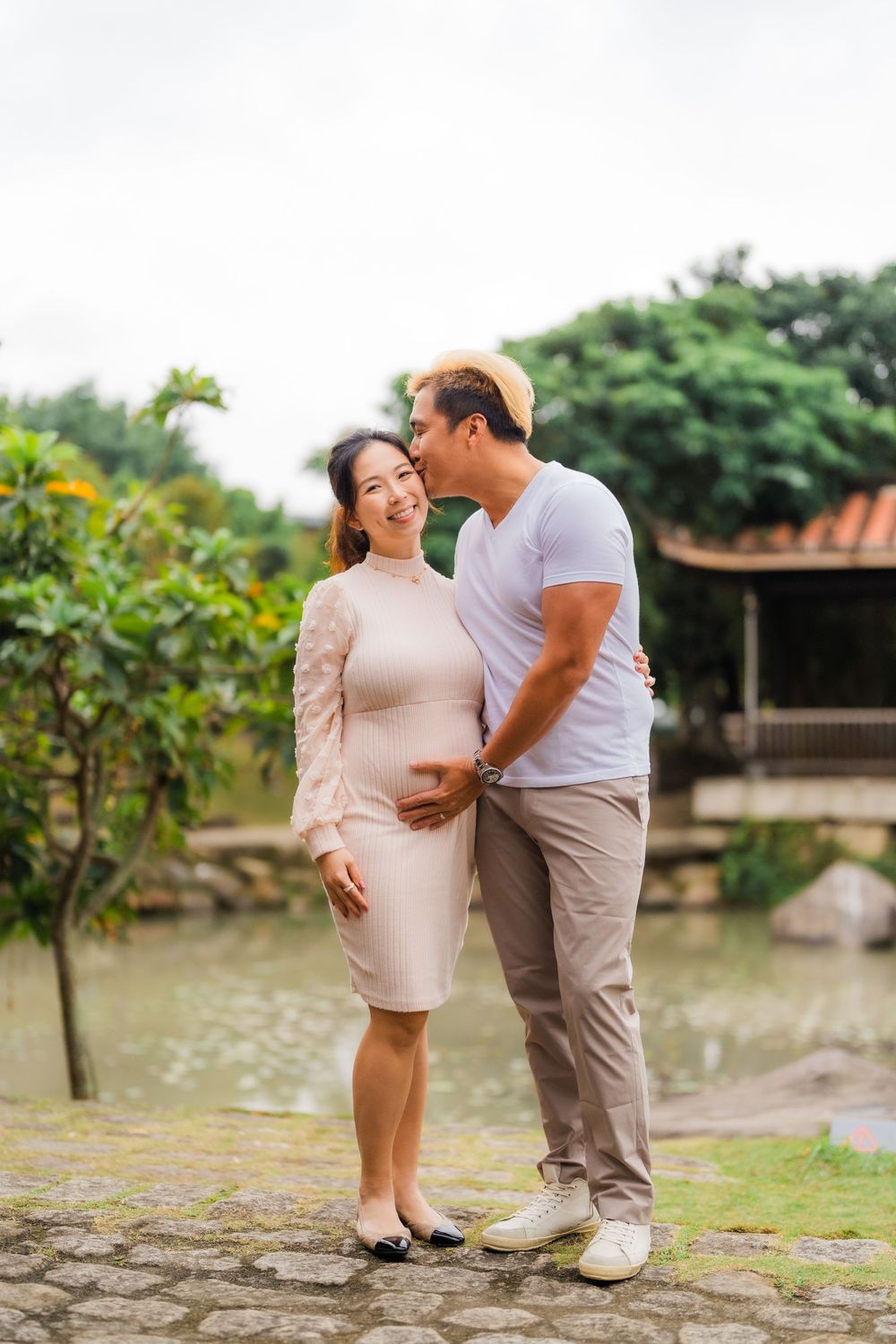 Couple embracing in a garden setting with traditional architecture in the background.