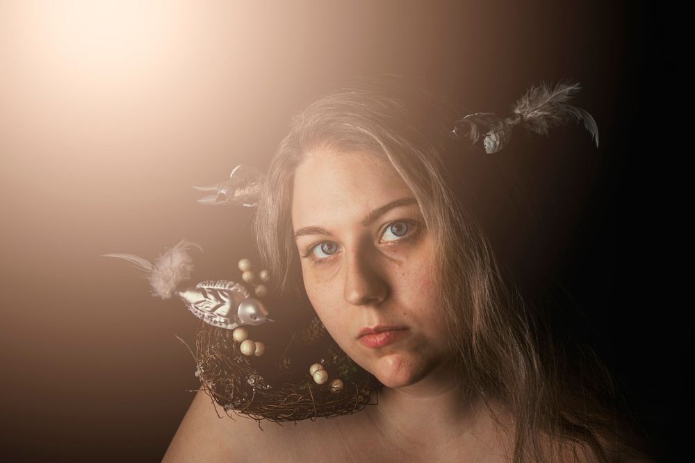 Ethereal portrait with soft lighting and floral elements against warm background.