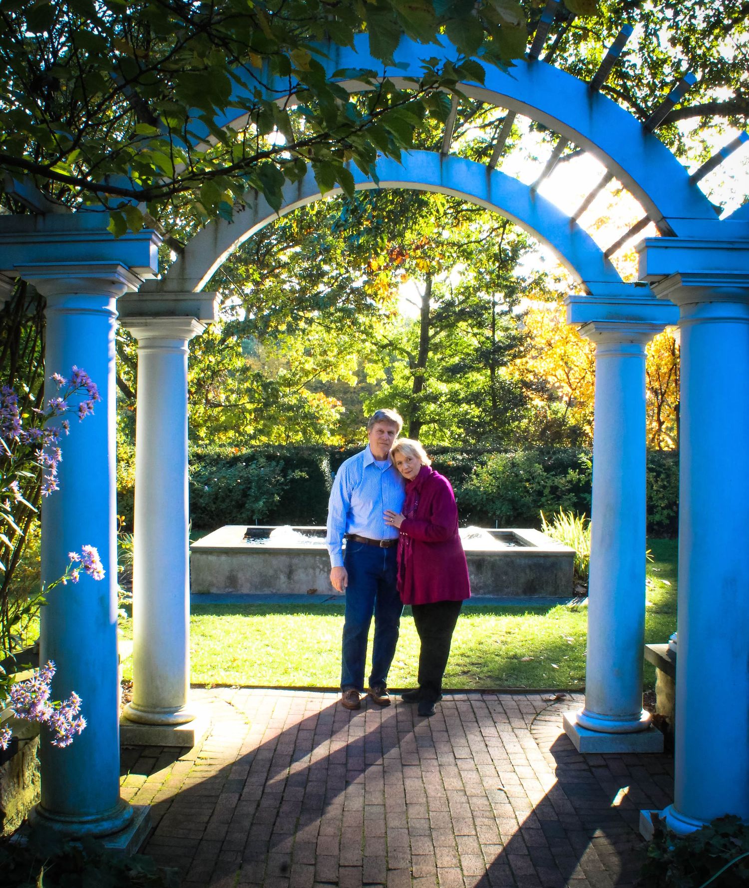 A couple sharing a moment under a blue garden archway with white columns.