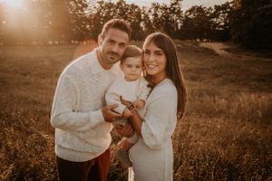 Warm sepia-toned family portrait session in a natural outdoor setting at sunset.