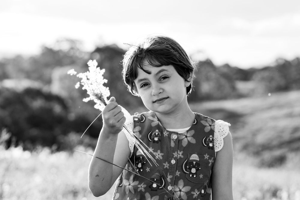 Black and white image of a child sitting in a field, holding a bouquet of wildflowers