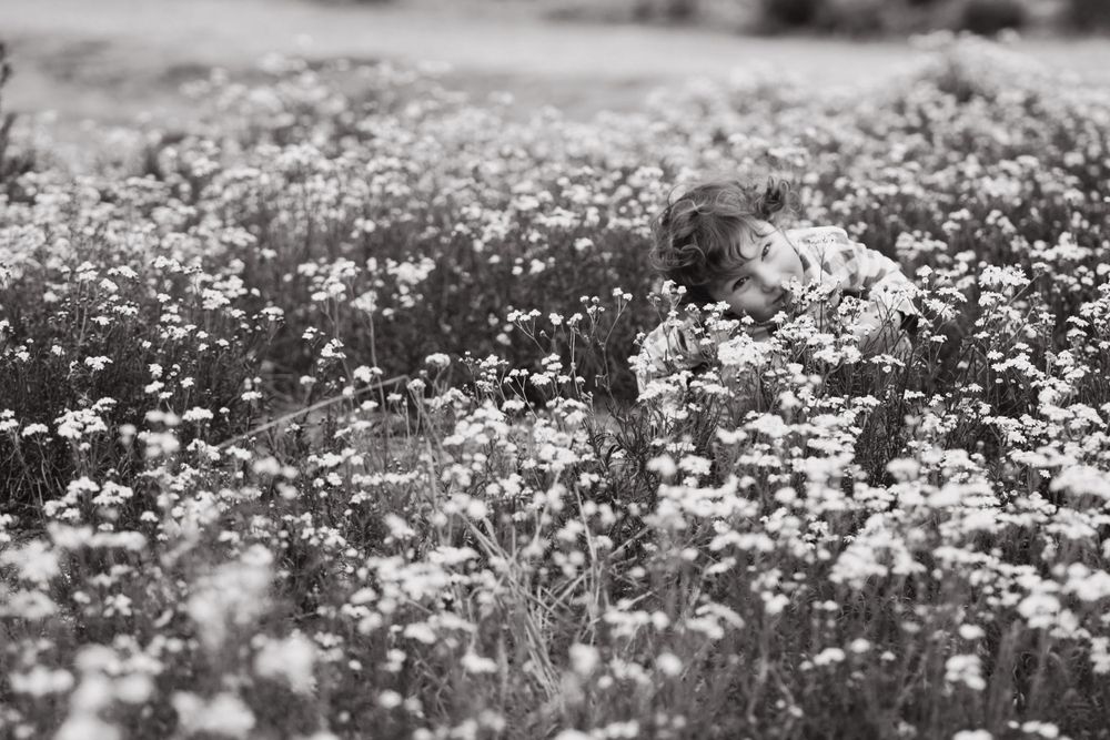 Black and white image of a child crouched among wildflowers
