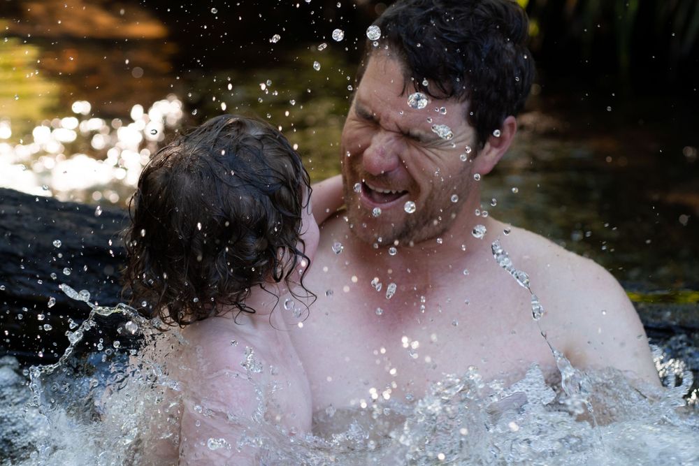 Young boy with curly hair, splashing in a creek with his father
