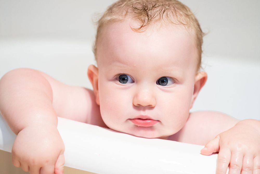 Baby boy peering over the edge of a bathtub