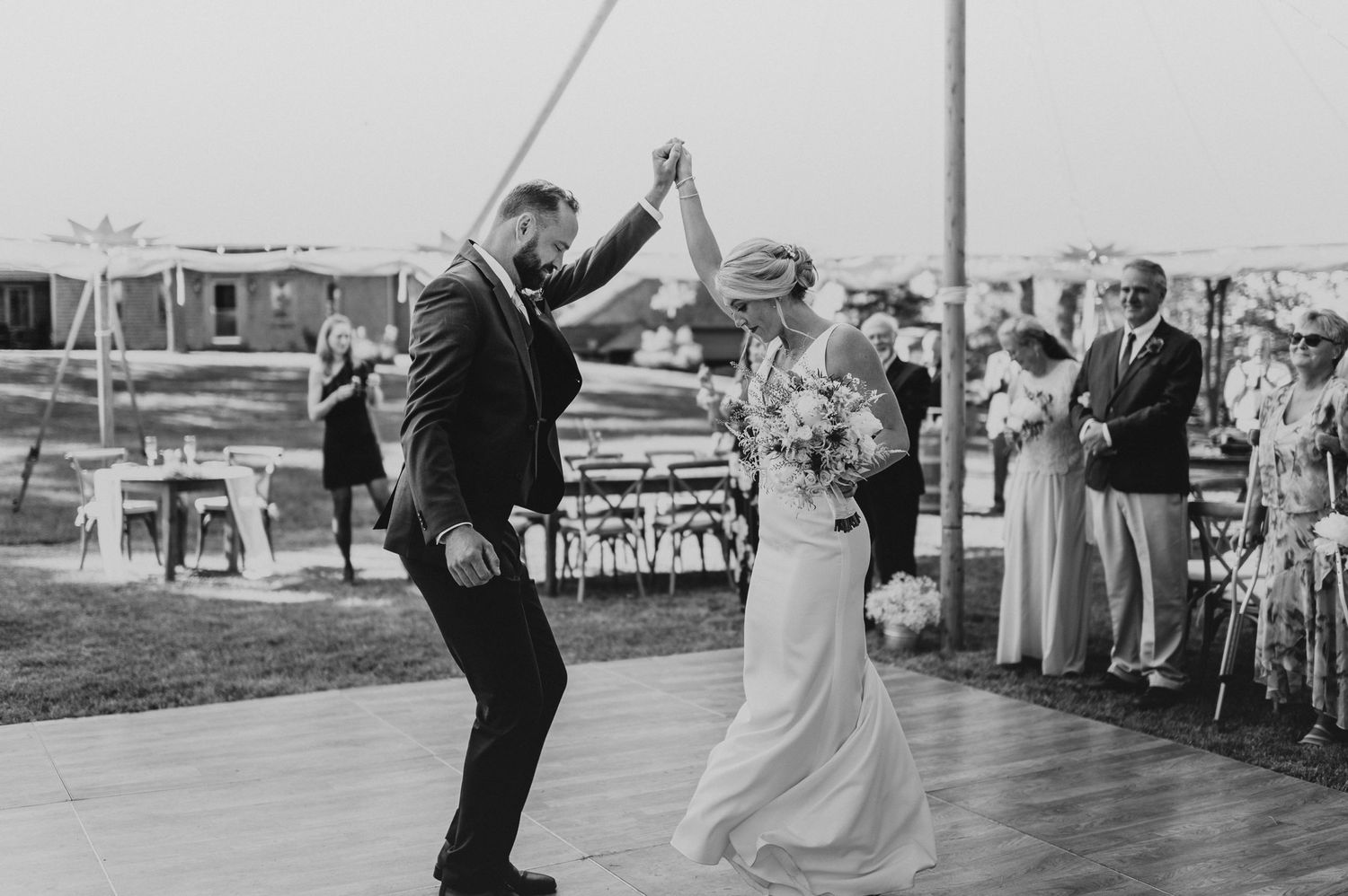Black and white photo of a lively dance celebration under a tent with guests watching.