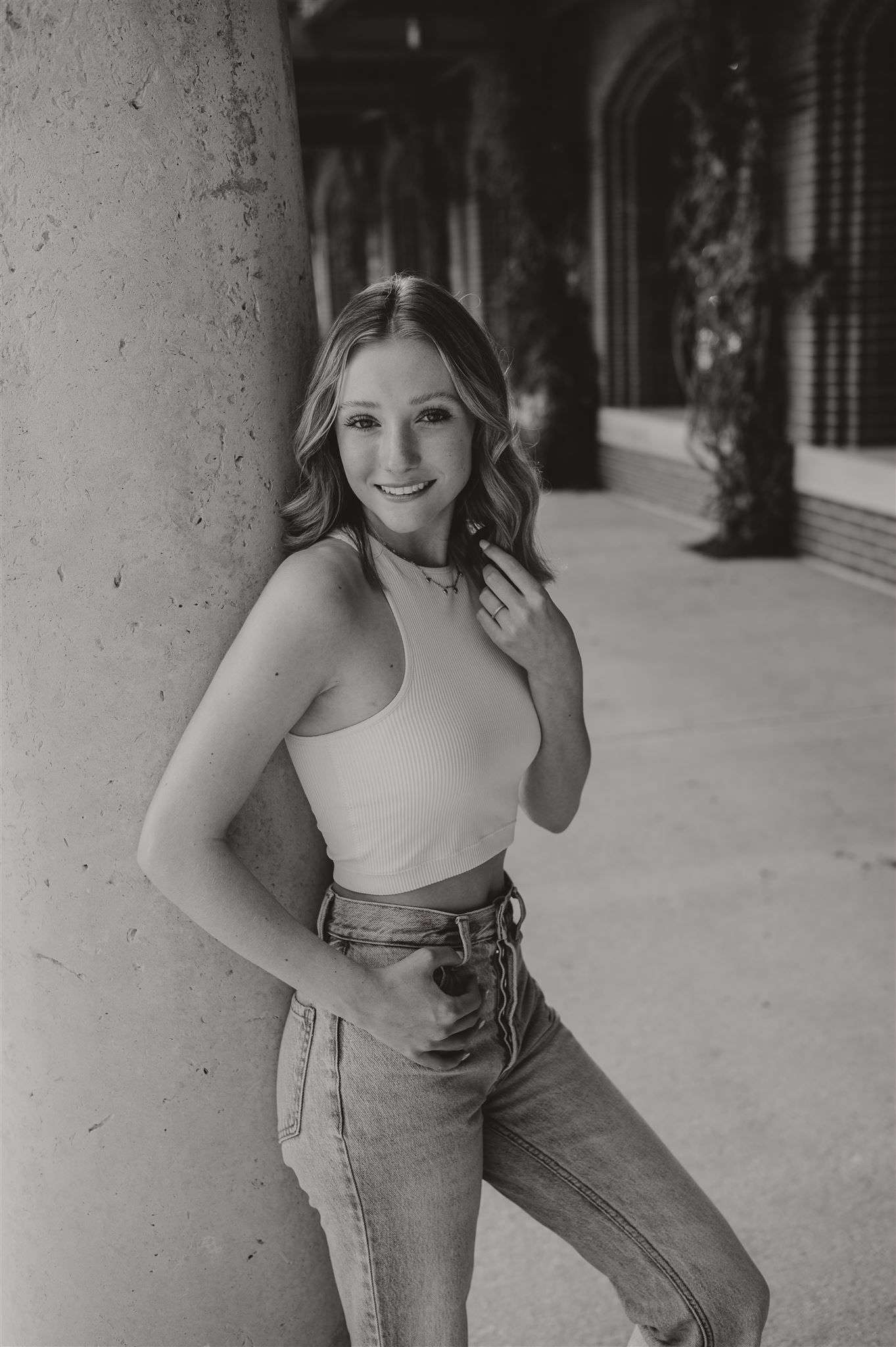 Black and white portrait against columns wearing a ribbed tank top and high-waisted jeans.