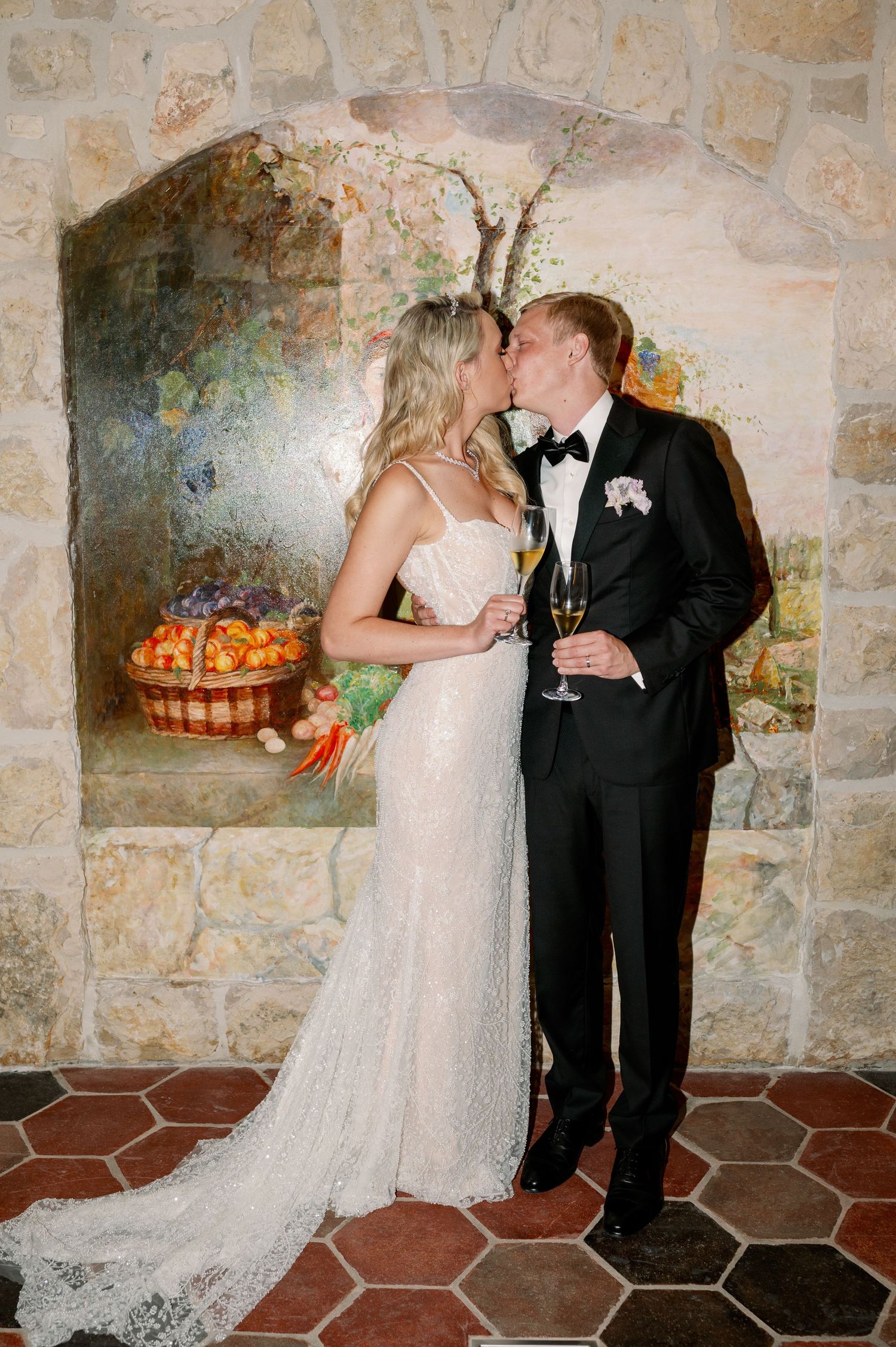 Romantic moment between newlyweds against stone wall with champagne.