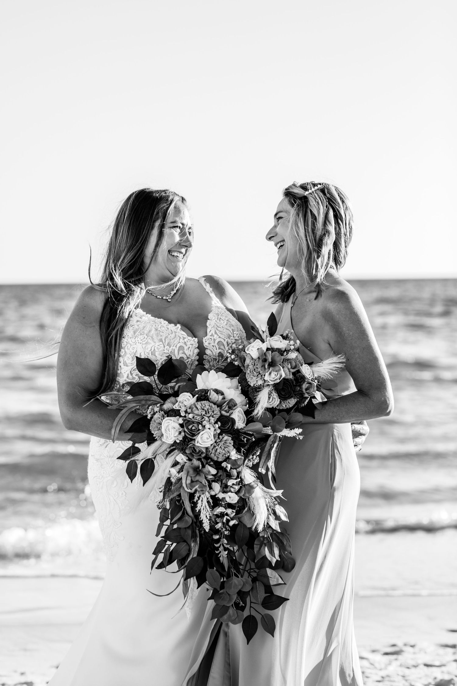 Black and white beach wedding photo showing joyful moment with bouquet of mixed flowers.