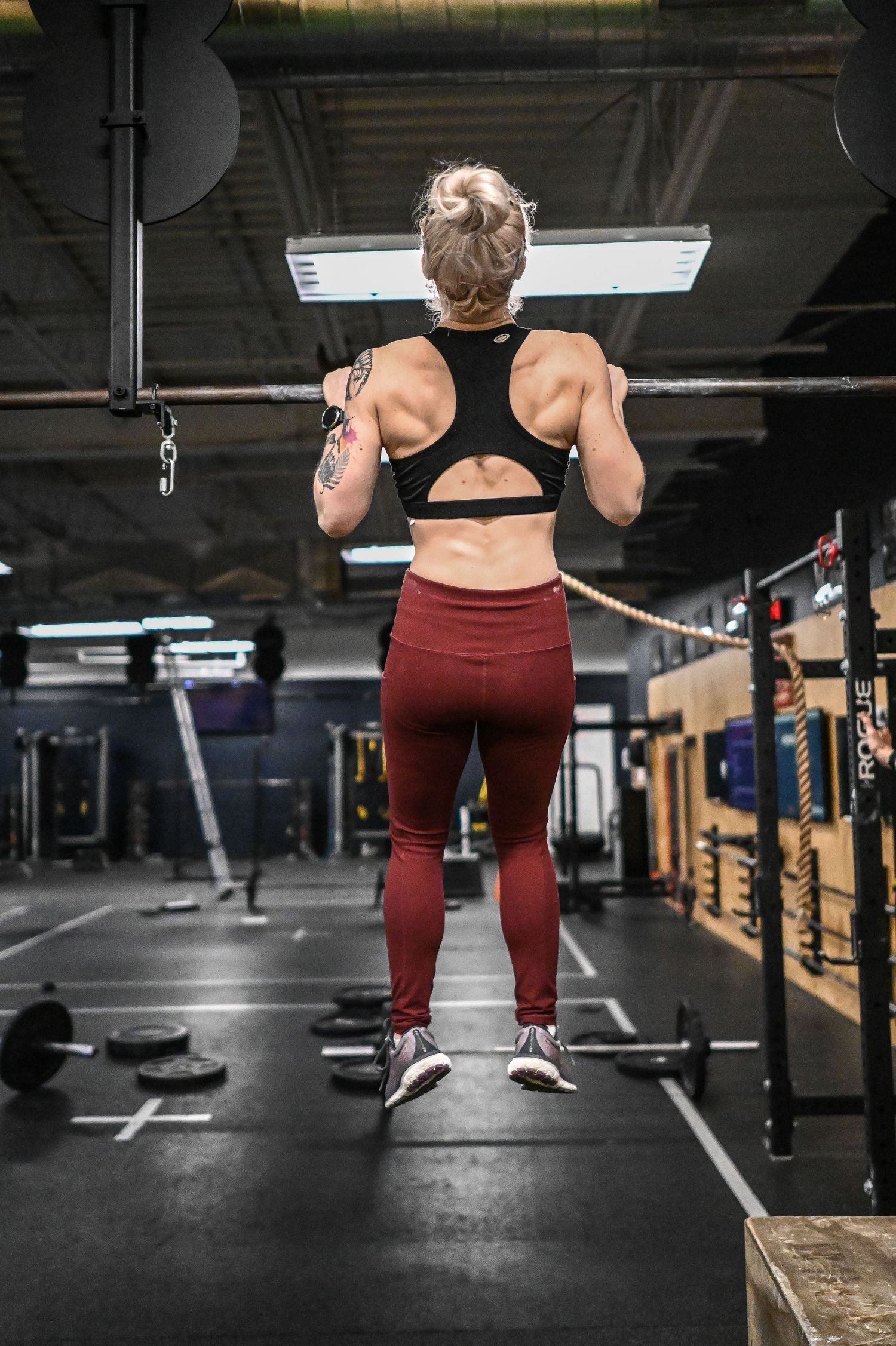 Athletic person performing squats with a barbell in a dimly lit gym setting.
