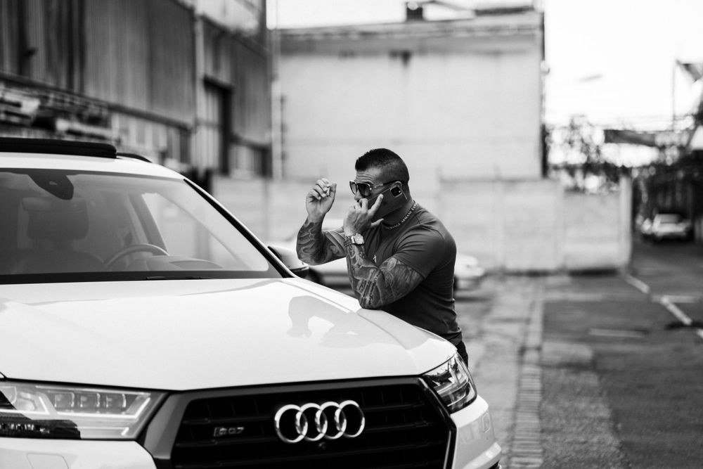Person in black clothing gesturing near white Audi car on urban street.