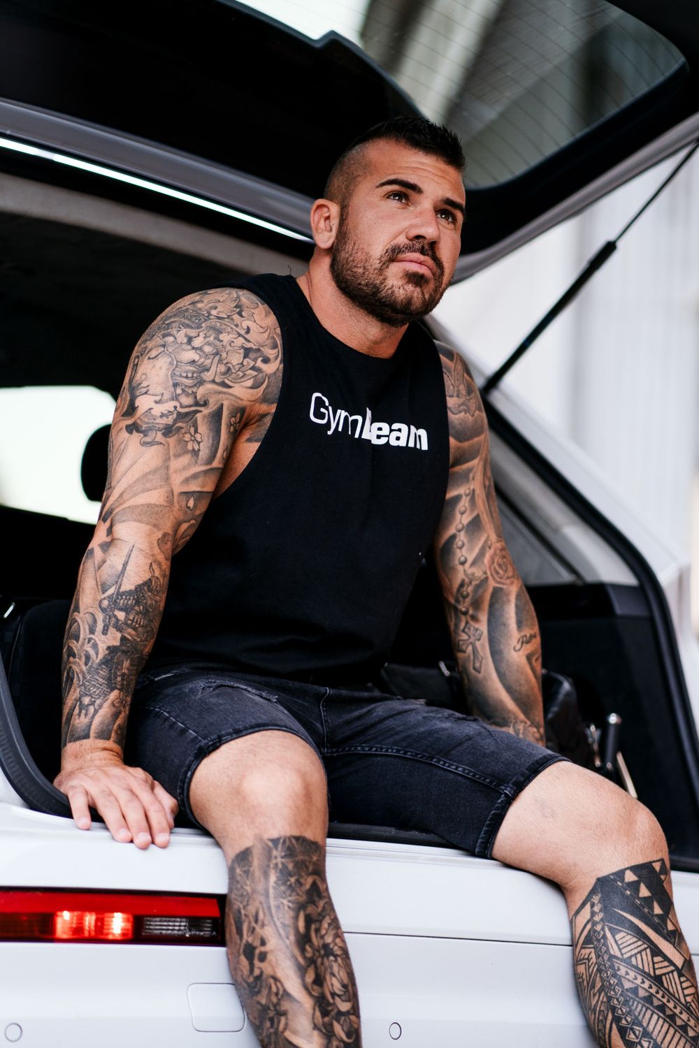 Tattooed person in black tank top sitting in white vehicle.