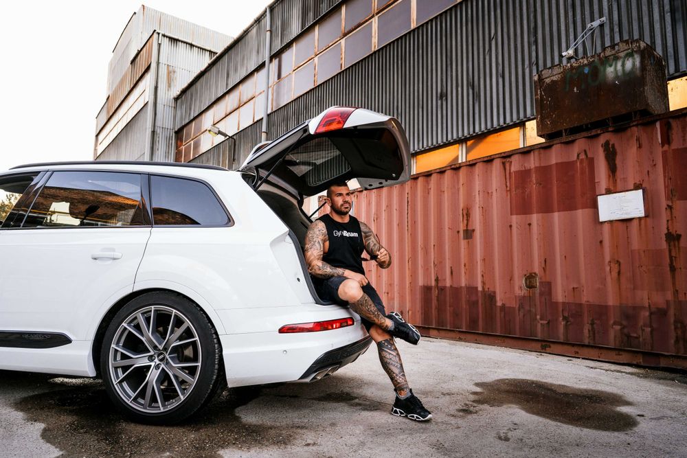Person sitting on open trunk of white luxury SUV near industrial building.