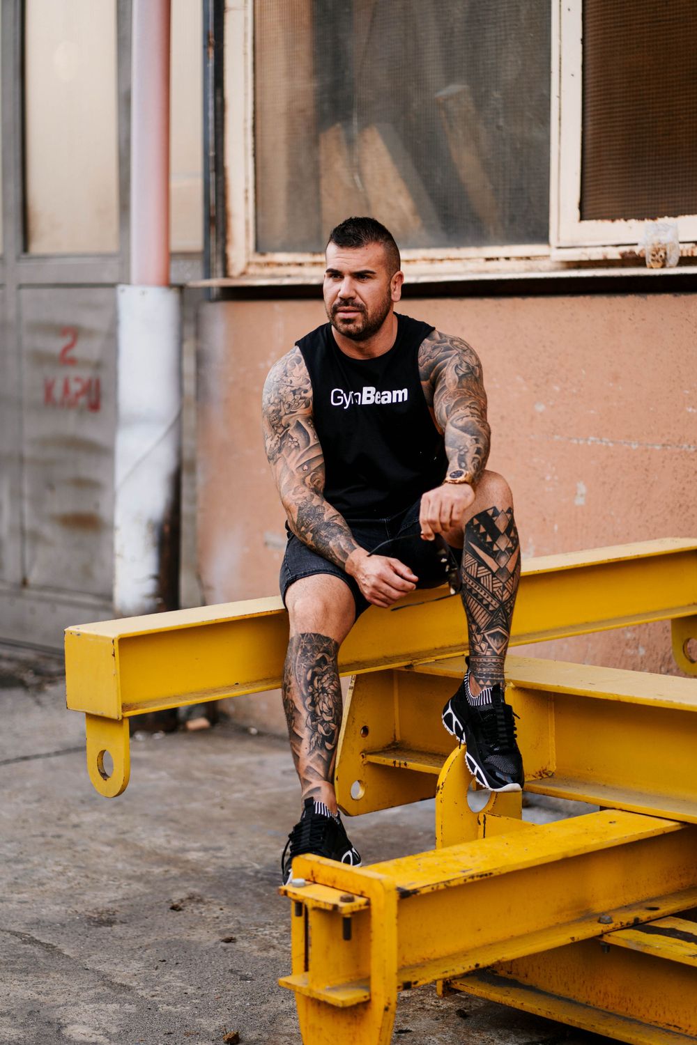 Person with tattoos sitting on yellow industrial equipment wearing black athletic wear.