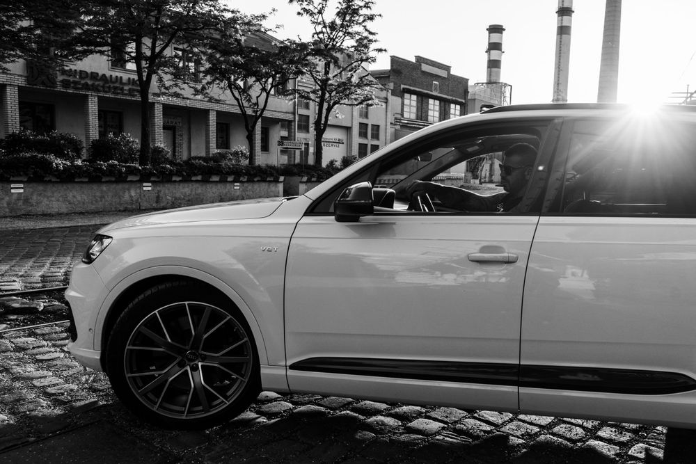 White Audi car parked on cobblestone street with industrial buildings in background.