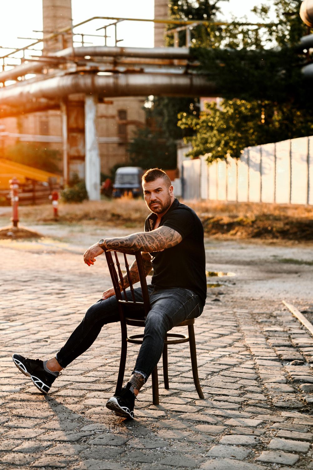 Silhouette seated on wooden chair against industrial backdrop during golden hour.