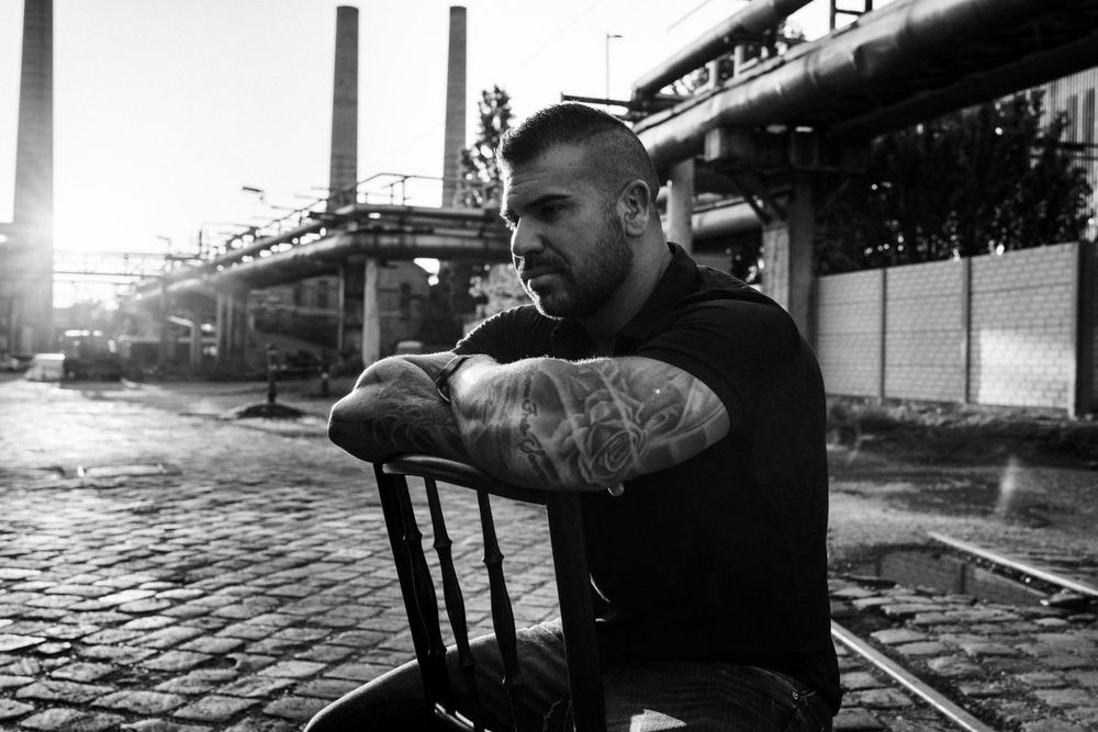 Monochrome image of person resting on chair with industrial structures in background.