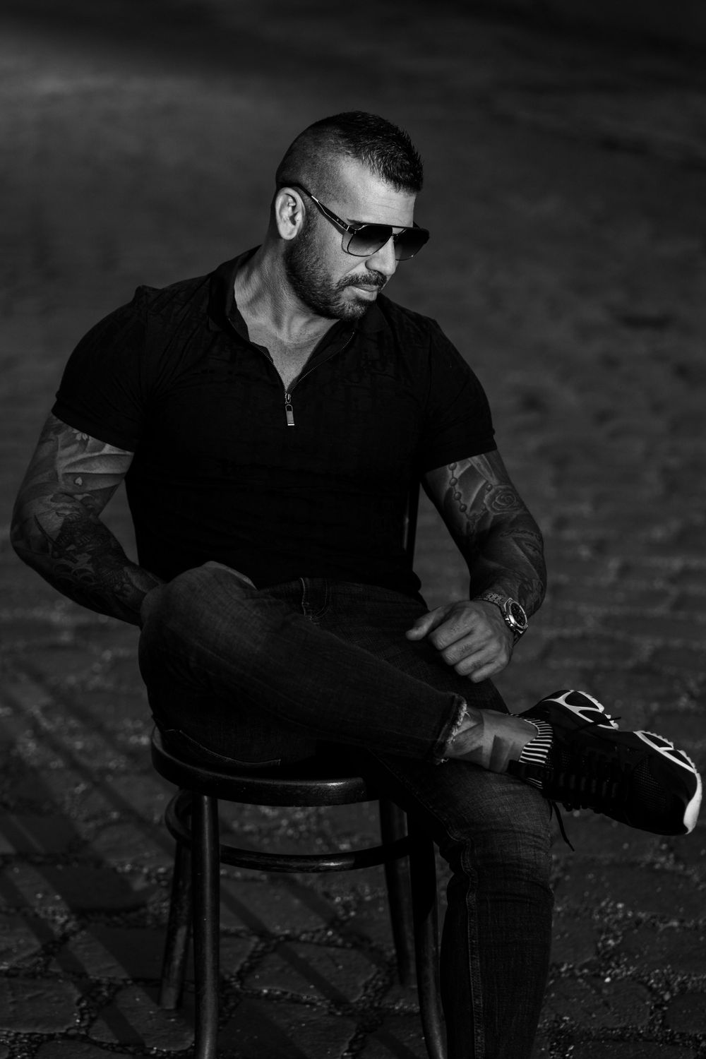Monochrome portrait of muscular person in black attire seated on wooden chair.